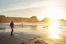 Vater mit Kind bei Sonnenuntergang am Strand von Big Sur, Kalifornien, USA
