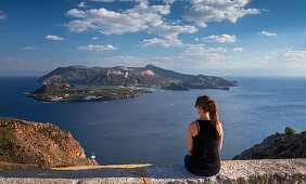 Lipari coast with woman sitting, looking at volcano island Vulcano at day, Sicily Italy