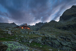 Dramatic clouds with illuminated Adolf Nossberger hut in the Gradental at night in the Hohe Tauern National Park, Austria