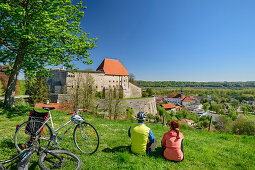 Woman and man cycling while taking a break in front of Burg Tittmoning, Tittmoning, Benediktradweg, Upper Bavaria, Bavaria, Germany