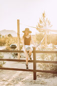 Woman sitting on fence in front of caravan in Joshua Tree National Park, Joshua Tree, Los Angeles, California, USA, North America