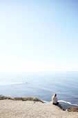 Junge Frau sitzt an einer Klippe und blickt auf den Pazifik am Rand des Highway 1, Big Sur State Park, Kalifornien, USA.