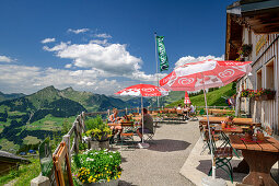 Gäste sitzen auf der Sonnenterrasse der Alpe Oberpartnun, Bregenzerwaldgebirge im Hintergrund, Biosphärenreservat Großes Walsertal, Lechquellengebirge, Vorarlberg, Österreich