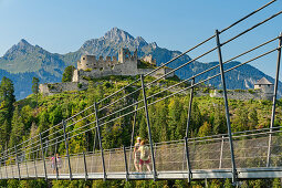 Several people walk over the Highline 179 rope bridge with Ehrenberg castle ruins in the background, Reutte, Tyrol, Austria
