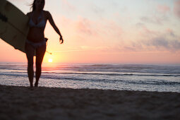 Female surfer goes with surfboard on the beach in sunset, surfing, Portugal, sunset