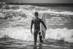 Surferin steht mit Surfbrett am Strand, Portugal