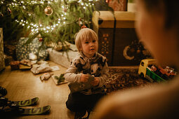 little boy unwraps his gifts in front of the Christmas tree, Christmas, family