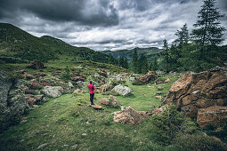 Woman stands on a rock and takes cell phone pictures of the red rocks at the red castle, Nockberge Biosphere Park, Carinthia, Austria, Europe.