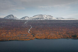 Landschaft mit verschneiten Bergen und Fluss zum See im Stora Sjöfallet Nationalpark im Herbst in Lappland in Schweden\n