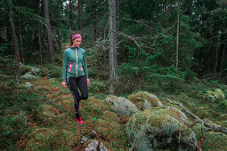 Frau wandert durch Wald mit Moos bedecktem Boden im Tyresta Nationalpark in Schweden\n