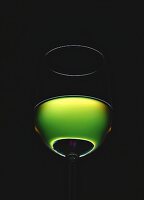 Filled white wine glass against green light