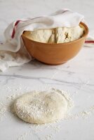 Pizza dough on marble slab and in bowl half-covered by tea towel