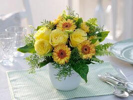 Gelber Blumenstrauss aus Rosen und Gerbera auf gedecktem Tisch