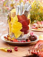 Autumn leaves and cutlery in glass (table decoration)