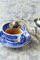 A cup of tea with silver teapot and tea strainer