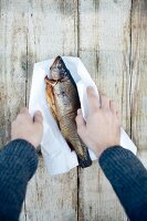 Hands holding grilled fish wrapped in paper