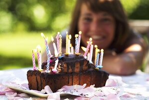 A birthday cake with burning candles and a young woman in the background