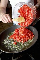 Woman Adding Fresh Diced Tomatoes into a Skillet on the Stove