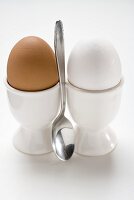 Brown and white eggs in eggcups, spoon between them