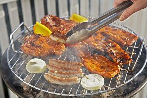 Meat, sausages and vegetables on barbecue, sausage in tongs