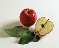 A whole red apple and half a red apple with leaves