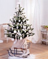 Weihnachtsbaum mit weißen Kugeln und Kerzen dekoriert, davor Vintage Schlitten und Schlittschuhen auf Holzboden