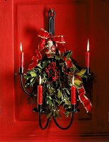 An roter Tür hängt ein Kerzenhalter mit Tollkirschen und Weihnachtsmann