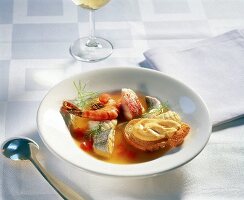 Fischsuppe mit Baguette und Würzpaste auf weißem Teller, Löffel