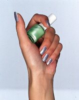 Frauenhand mit gruen lackierten Naegeln hält Nagellackflasche