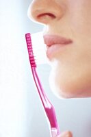 Side view of woman massaging her lips with pink toothbrush, close-up