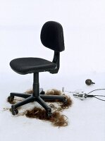Brown hair lying on floor under dark chair with hairstyling equipments