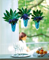 Blaue Hängevasen gefüllt mit Enzian- stielen und einem Aralienblatt
