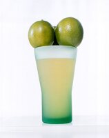 Glass of lime juice with whole lemons on top on white background