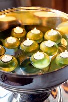Burning tea light candles in green apples floating in silver bowl