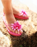 Frauenfüße in rosafarbenen Flip-Flops mit Stoffblüte