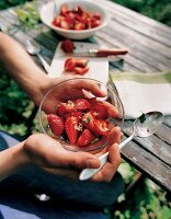 Hände halten eine Schale marinierter Erdbeeren mit Waldmeister