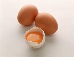 Zwei ganze braune Hühnereier, 1/2 weißes Ei mit Eigelb