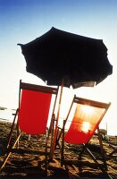 Zwei leere Sonnenstühle unter Sonnen schirm am Meeresstrand