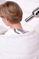 Hair dryer being blowed on aluminium foil placed on blonde woman's shoulder