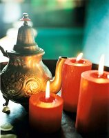 Oriental teapot besides orange lit candles