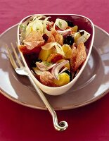 Potato salad with salami, olives, dried tomatoes and onions in bowl