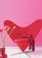 Red heart shaped chair with hand bag and scarf against pink background
