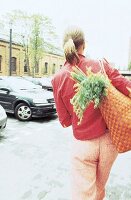Frau geht mit Einkaufstasche über der Schulter Richtung Auto