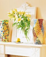 Flowers in glass vase, colourful mosaic lanterns and mirror on mantelpiece