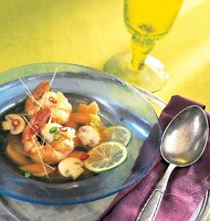 Spicy prawn soup with chilli, ginger, mushrooms and lemon wedges in blue serving dish