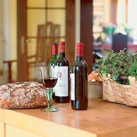 Bauernbrot, Rotweinflaschen, Glas Rotwein auf Holztisch