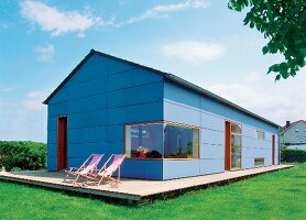 Niedrigenergiehaus aus Holz, blau, auf Betonplatte im Grünen