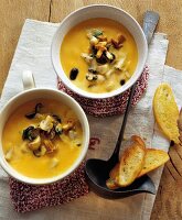 Pumpkin soup with mushroom and toast in two soup bowls on white cloth
