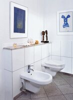 Bad, WC daneben ein Bidet, beides an der weiß gefliesten Wand befestigt