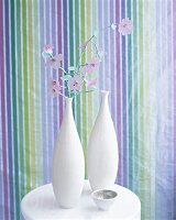 Zwei bauchige weiße Vasen mit Kunstblumen vor Streifentapete